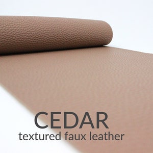 May include: A roll of cedar-colored textured faux leather. The material is a warm brown with a subtle, pebbled texture. The text "CEDAR" and "textured faux leather" are displayed in black.