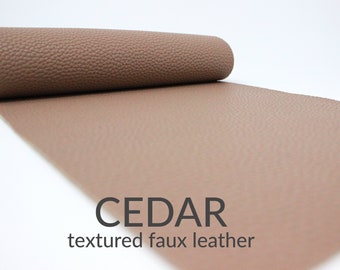 May include: A roll of cedar-coloured textured faux leather. The material is a warm brown with a subtle, pebbled texture. The text "CEDAR" and "textured faux leather" are displayed in black.
