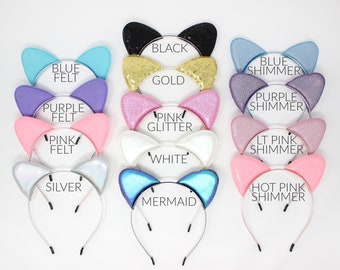 Puede incluir: Diez diademas de orejas de gato diferentes con varios colores y texturas. Las diademas están hechas de fieltro, purpurina y brillo. Los colores incluyen negro, dorado, azul, morado, rosa, blanco, plateado y rosa intenso.