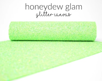May include: A roll of light green glitter canvas fabric. The fabric is sparkly and has a subtle iridescent sheen. The text "honeydew glam glitter canvas" is printed above the fabric.