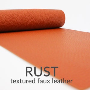 May include: A roll of textured faux leather in a rust colour. The leather has a pebbled texture. RUST textured faux leather.
