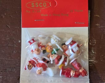 May include: A package of 16 plastic Christmas ornaments featuring Santa Claus figures in various poses. The ornaments are white with red accents and have a small hole at the top for hanging. The package is labeled "SSCO No. 314 Made in Hong Kong".