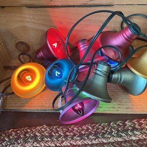 May include: A string of colorful, bell-shaped lights in shades of red, blue, orange, and purple. The lights are strung on a black wire and are arranged in a wooden box. The lights have a vintage, retro aesthetic.
