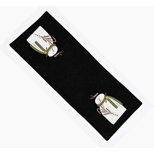 May include: Black rectangular table runner with embroidered snowmen. The snowmen have white bodies, green scarves, and red and white candy cane accents. A festive holiday decoration.