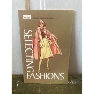 May include: A vintage Sears "Selecting Fashions" book cover. The cover features an illustration of a woman in a pink coat and hat, a cream-colored skirt suit, and red shoes. The book title is in large white letters.