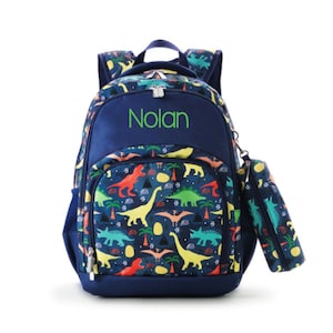 May include: A blue backpack with a dinosaur print and a matching pencil case. The backpack has a name tag that says "Nolan".