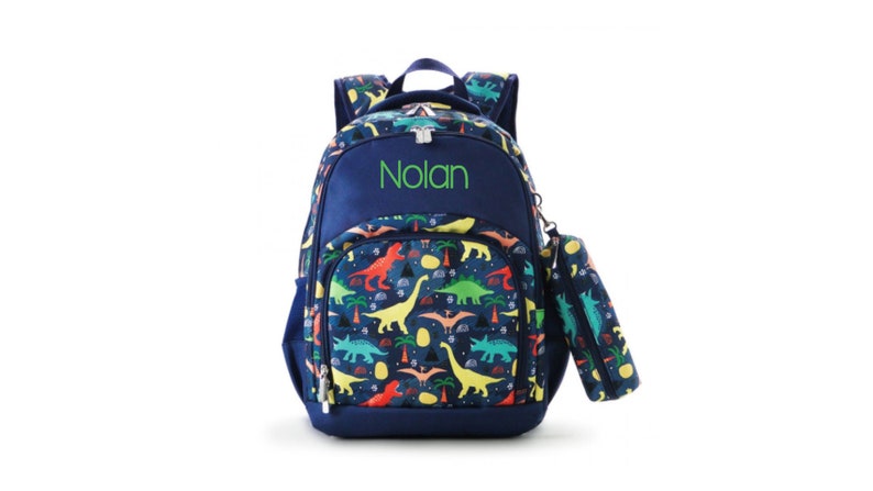 May include: A blue backpack with a dinosaur print and a matching pencil case. The backpack has a name tag that says "Nolan".