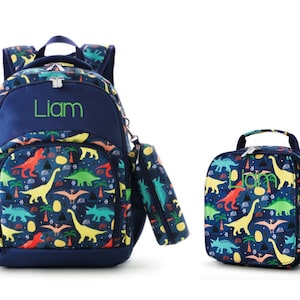 May include: A blue backpack and lunch bag set with a dinosaur print. The backpack has a zippered pocket and a name tag that says "Liam".