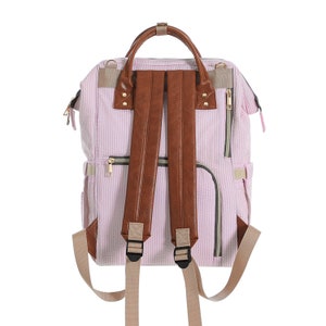 May include: Pink and white striped diaper bag with brown leather straps and gold zippers. The bag has a top handle and adjustable shoulder straps.