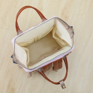 May include: A pink and brown diaper bag with multiple pockets and compartments. The bag has a zipper closure and a top handle. The bag is open and empty, showing the interior lining.