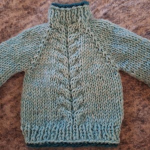 May include: A light blue knitted sweater with a cable knit pattern and a high neck.