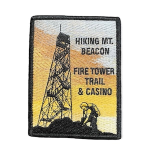 May include: An embroidered patch featuring a black silhouette of a fire tower on a yellow and orange sunset background. The text "Hiking Mt. Beacon Fire Tower Trail & Casino" is embroidered in black.
