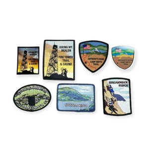 May include: Ten embroidered patches featuring various hiking trails and landmarks. The patches are beige, brown, blue, and green with white text. The text includes "Hiking Mt. Beacon", "Fire Tower Trail & Casino", "Anthony's Nose Camp Smith Trail", "Stone Chambers Putnam County, NY", "Storm King", and "Breakneck Ridge".