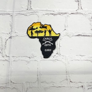 May include: Black and yellow embroidered patch shaped like the continent of Africa. The patch features a sunset scene with silhouettes of people and a tree. The text "CHAOS 69TH EARF" is embroidered in white on the patch.