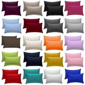May include: A collection of twenty rectangular pillowcases in various solid colors, including purple, beige, black, magenta, light blue, dark red, charcoal, gray, brown, cream, orange, lavender, lime green, navy, yellow, pink, red, teal, white, and blue.