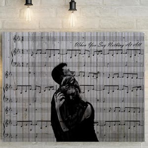 May include: A black and white illustration of a couple embracing on a sheet music background. The music sheet has the title "When You Say Nothing At All".