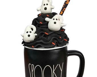May include: A black mug with the word "SPOOKY" in white script. The mug is topped with black frosting, orange sprinkles, and three white ghost figurines. A black and orange straw is inserted into the frosting.