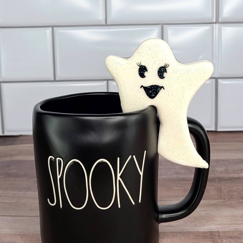 This Pink Glam Halloween Mug Hugger is a fake, decorated cookie in the shape of ghost (check out her face) that hugs the rim of a mug with a notch cut on the side. 

This Mug Hugger Cookie looks so real but it is made from non-edible product.