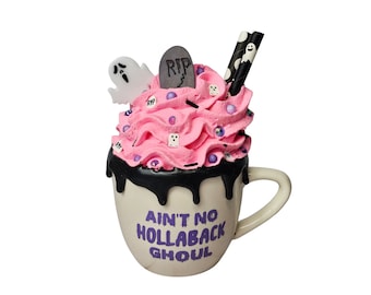 May include: A white ceramic mug with black dripping icing and pink and purple frosting. The mug has the text "Ain't No Hollaback Ghoul" in purple lettering.