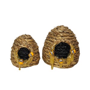 May include: Two beehive-shaped decorations made of woven straw with a black entrance and dripping honey. The beehives are decorated with small yellow and black bees.