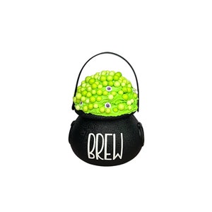 May include: A black cauldron with a green, bubbly substance and purple eyes. The cauldron has a black handle and the word "BREW" in white lettering on the front. A Halloween-themed decoration.