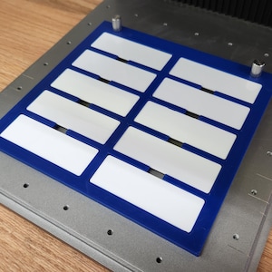 May include: A blue and white rectangular template with nine blank spaces for labels. The template is on a silver surface with small holes.