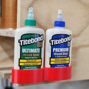 May include: Two bottles of Titebond wood glue, one labeled "Ultimate" and the other labeled "Premium", are held in a red plastic holder mounted on a wooden surface.