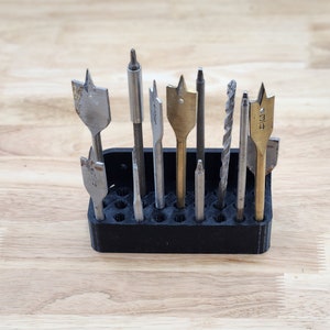 May include: A black plastic drill bit holder with a variety of drill bits, including wood drill bits, metal drill bits, and spade drill bits.