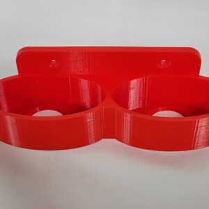 May include: A red plastic wall-mounted holder with two circular openings for holding items.