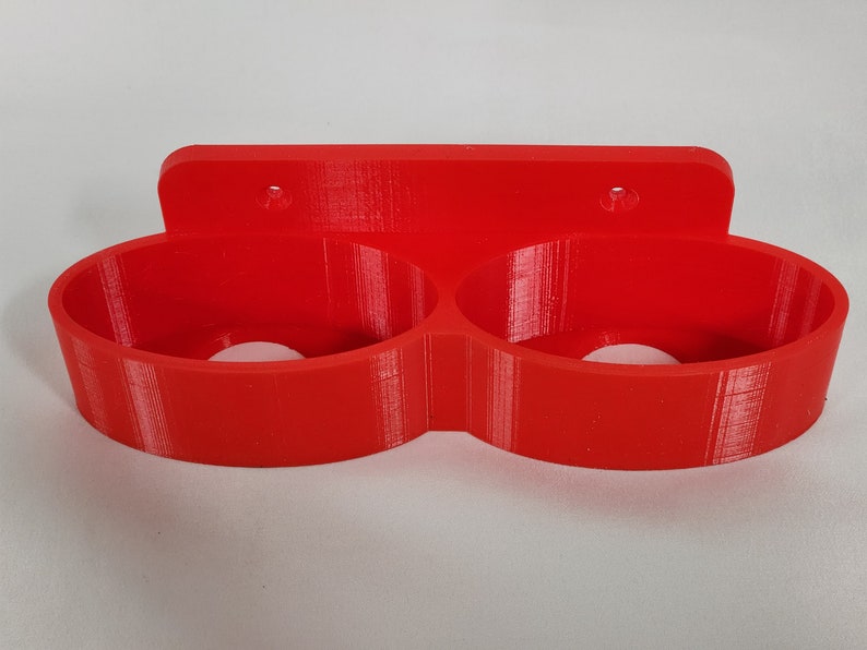 May include: A red plastic wall-mounted holder with two circular openings for holding items.