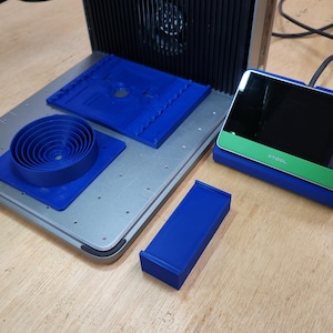 May include: An assortment of blue 3D-printed components and a digital display device. The components include a series of concentric circles, a rectangular piece, and a tray with a ridged design. The display has a green accent and a black screen.