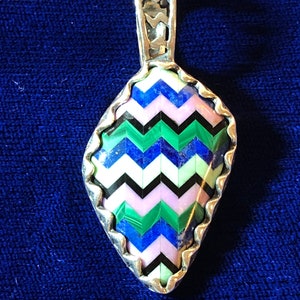 Puede incluir: Un colgante de plata con un dise&ntilde;o geom&eacute;trico que presenta una variedad de piedras de colores, incluyendo azul, verde, rosa y negro.