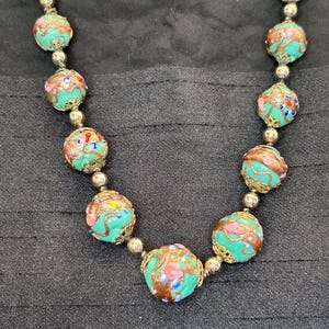 May include: A turquoise necklace with gold accents and colorful floral patterns on each bead.