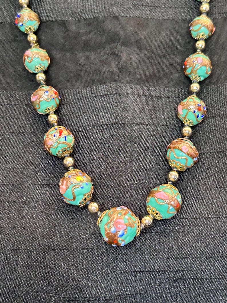 May include: A turquoise necklace with gold accents and colorful floral patterns on each bead.