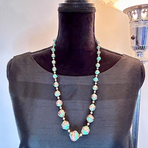 May include: A turquoise and pink beaded necklace with gold accents. The beads are round and have a floral design. The necklace is on a black mannequin.