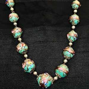 May include: A turquoise and gold necklace with round beads. The beads are decorated with intricate floral patterns and colorful accents.