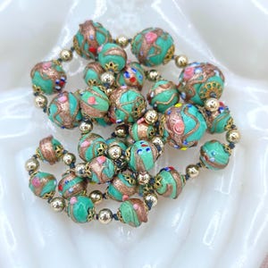 May include: A vintage necklace made of turquoise blue glass beads with gold and silver accents. The beads are decorated with intricate patterns and colorful details.