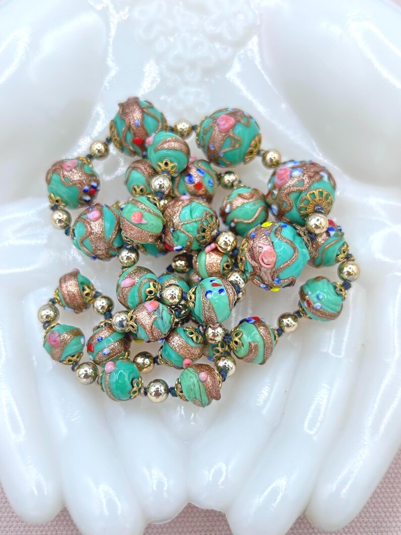 May include: A vintage necklace made of turquoise blue glass beads with gold and silver accents. The beads are decorated with intricate patterns and colorful details.