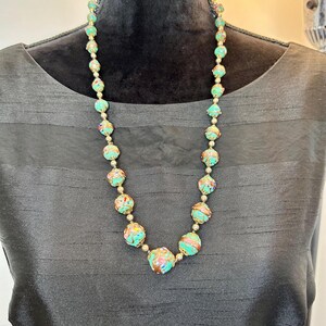 May include: A turquoise and gold necklace with round beads. The beads are decorated with a swirling pattern of gold and pink.