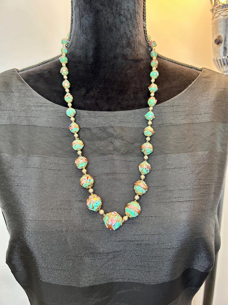 May include: A turquoise and gold necklace with round beads. The beads are decorated with a swirling pattern of gold and pink.