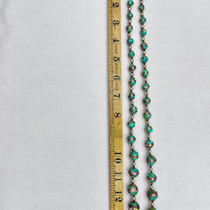 May include: A turquoise and gold beaded necklace with a silver clasp. The necklace is approximately 14 inches long and features intricate details on each bead.