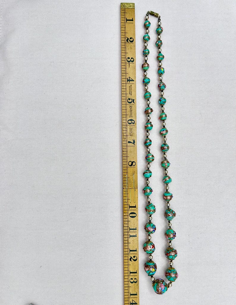 May include: A turquoise and gold beaded necklace with a silver clasp. The necklace is approximately 14 inches long and features intricate details on each bead.