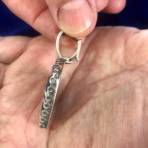Puede incluir: Un colgante de plata con un dise&ntilde;o redondo de esmalte multicolor. El colgante tiene un borde texturizado detallado y un bucle de plata para sujetar una cadena.