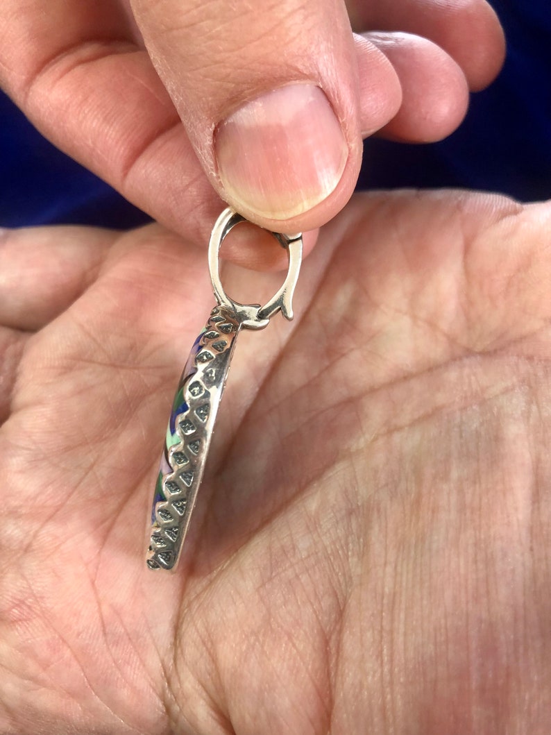 Puede incluir: Un colgante de plata con un dise&ntilde;o redondo de esmalte multicolor. El colgante tiene un borde texturizado detallado y un bucle de plata para sujetar una cadena.