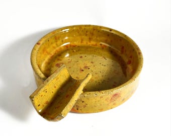 May include: A yellow ceramic ashtray with a speckled glaze and a built-in cigar rest.