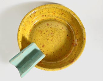 May include: A yellow ceramic bowl with a speckled glaze and a light blue ceramic slide inside. The bowl is round and shallow, and the slide is small and curved.