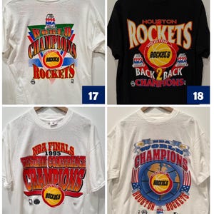 May include: Four vintage Houston Rockets t-shirts. The first shirt is white with red, green, and blue text that says "World Champions" and "Rockets". The second shirt is black with red, yellow, and white text that says "Houston Rockets" and "Back 2 Back Champions". The third shirt is white with red, yellow, and blue text that says "NBA Finals 1995 Western Conference Champions" and "Rockets". The fourth shirt is white with red, blue, and yellow text that says "World Champions" and "Houston Rockets".