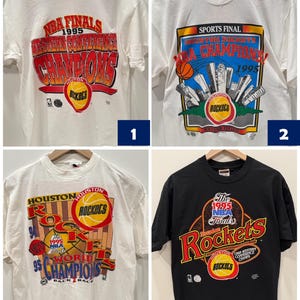 May include: Four vintage Houston Rockets t-shirts. The first two are white with red, blue, and yellow graphics. The third is white with red, blue, yellow, and black graphics. The fourth is black with red, blue, yellow, and white graphics.