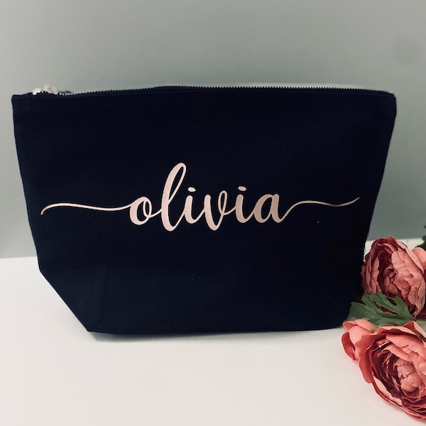 May include: A navy blue make-up bag with a zip. The name "olivia" is printed in rose gold script on the front. Pink flowers are in the background.