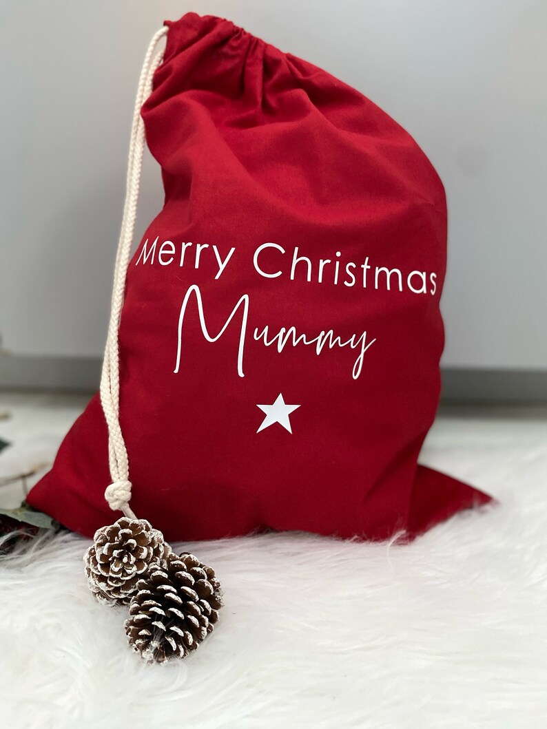 Puede incluir: Bolsa de regalo roja de Navidad con cord&oacute;n de ajuste blanco y el texto "Merry Christmas Mummy" y una estrella blanca.